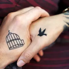 Zwei Hände mit leichten Tattoos zum selber zeichnen: Ein Vogel fliegt aus einem Käfig.