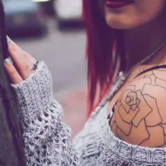 Dezent blühendes Tattoo Schulter Frau, eine zarte Rose ziert ihre Haut, umrahmt von einem Strickpullover.