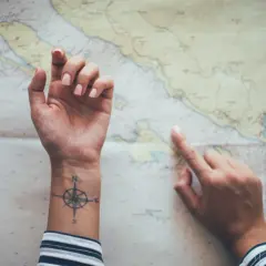 Hände über einer Seekarte, eine mit einem Kompass-Tattoo, das an ein Partner Tattoo Koordinaten erinnert.