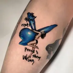 Ein Fineline Tattoo zeigt eine Frau mit Flügeln, die auf einem blauen Ballon sitzt. Darunter steht "Play them right, Prove them wrong".
