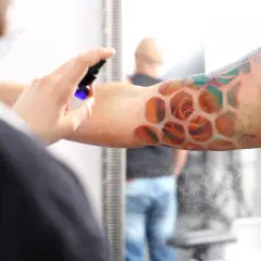 Ein frisches Tattoo mit Rosen in Wabenform wird besprüht. Der Träger ruht sich aus, während die Pflege beginnt.