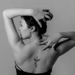 Rückenansicht einer Frau mit einem Phönix-Tattoo, einem der beliebten Tattoos. Ihre Hände sind im Haar und am Nacken.