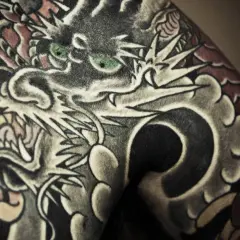 Ein detailreiches Irezumi Tattoo zeigt einen Drachenkopf mit grünen Augen, der sich über die Haut schlängelt.
