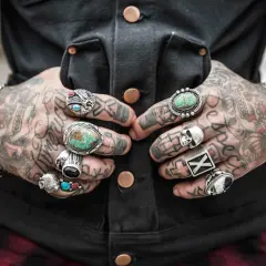 Tätowierter Mann mit vielen Ringen an den Fingern, darunter ein Totenkopf und Türkise.