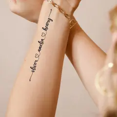 Ein zartes **Enkel Tattoo Namen** zeigt "oliver & amelia & henry" in geschwungener Schrift auf einem Arm, geschmückt mit einem goldenen Armband.