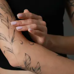 Ein frisches Tattoo mit Blattmotiven ziert den Arm einer Person, die schwarze Kleidung trägt.