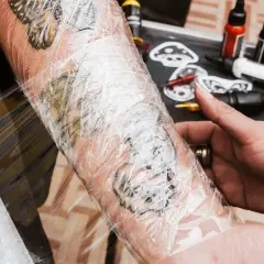 Frisch gestochenes Tattoo wird mit Tattoo-Folie geschützt. Die Folie schmiegt sich eng an, sodass keine Luft darunter ist.