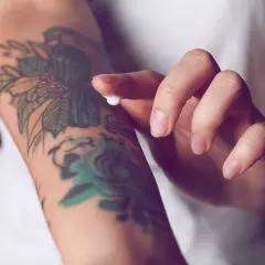 Hand testet Tattoo-Creme auf einem bunten Arm-Tattoo.