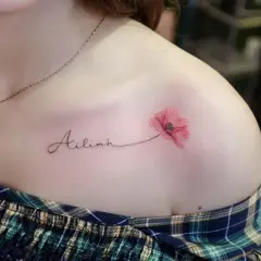 Ein zartes Tattoo mit dem Namen "Ailinh" und einer roten Mohnblume auf der Schulter.