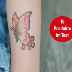 Ein buntes Schmetterlings-Tattoo mit 16 Jahren auf dem Arm. Daneben ein roter Kreis mit der Aufschrift "15 Produkte im Test".
