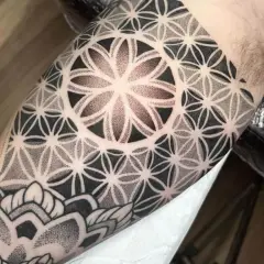 Ein Mann trägt ein geometrisches Tattoo am Oberarm. Das Muster erinnert an eine Blume des Lebens und ist fein gestochen.