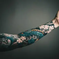 Ein Arm voller Tätowierungen: eine Schlange, Blumen und ein Gesicht. Die sleeve tattoo kosten sind hoch, aber die Kunst ist es wert.