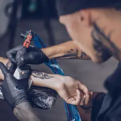 Ein Mann erhält ein intimtattoo am Arm. Der Tätowierer arbeitet sorgfältig mit der Maschine.