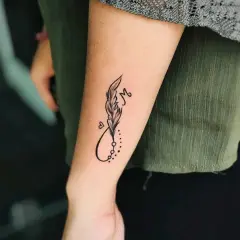 Ein kleines Feder-Tattoo mit Unendlichkeitszeichen und dem Buchstaben M auf dem Unterarm eines Mannes.