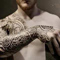 Mann mit beeindruckenden Sleeve Tattoo Ideen, die sich über Arm und Schulter erstrecken. Geometrische Muster und geschwungene Linien.