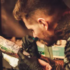 Ein Tätowierer mit vielen Rapper-Tattoos sticht einem Kunden ein neues Motiv auf den Arm.