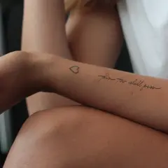 Ein Tattoo auf dem Unterarm einer Frau mit der Aufschrift "this too shall pass" und einem kleinen Herz. Ein Symbol der Hoffnung nach der Überwindung von Alkoholsucht.