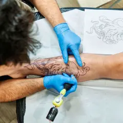 Tätowierer mit blauen Handschuhen sticht Oktopus-Motiv auf Bein. Tolle Tattoo-Ideen für Meeresliebhaber.