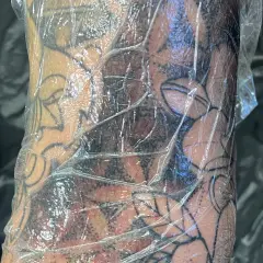 Frische Tattoo-Haut geht ab, bedeckt mit Folie. Das Motiv zeigt dunkle Schattierungen und klare Linien.