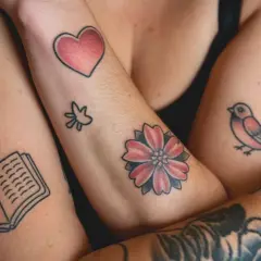 Viele kleine Tattoos am Arm eines Mannes: ein Herz, ein Vogel, eine Blume, ein Buch und Zweige.