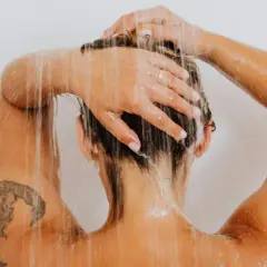 Frauenkopf unter der Dusche, Wasser rinnt über Schultern und Arme mit einem frischen Tattoo.