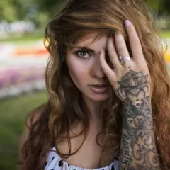 Frau mit welligem Haar und einem detaillierten Mandala Handgelenk Tattoo, das sich über ihren Unterarm erstreckt.