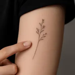 Zarter Zweig als Fineline Tattoo am Handgelenk. Ein Finger berührt sanft die Haut neben dem filigranen Motiv.