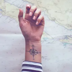 Ein Handgelenk mit einem Kompass-Tattoo, das die Verbundenheit von Geschwistern symbolisiert, vor einer Seekarte.