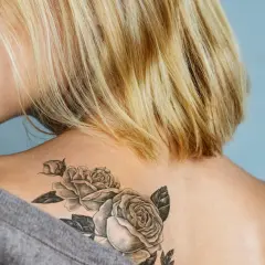 Blonde Frau mit einem Rosen-Tattoo ohne Folie auf der Schulter.