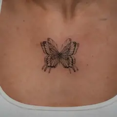 Zartes Fineline-Tattoo eines Schmetterlings zwischen den Brüsten, das wie ein filigranes Kunstwerk wirkt.