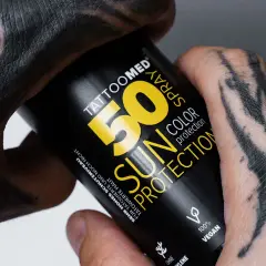 Hände mit Tattoos halten eine Sonnencreme-Spraydose. Die Dose schützt die Haut und das Tattoo vor der Sonne.