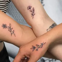 Drei Arme zeigen zarte, elegante Tattoos von Blumen und Zweigen.