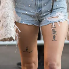 Ein Oberschenkel Tattoo Schriftzug mit einer Rose und einer stilisierten Figur.