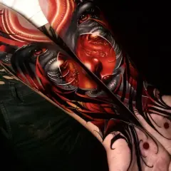 Arm-Tattoos mit roten Tattoos, die ein dämonisches Gesicht mit roten Augen und scharfen Zähnen darstellen.