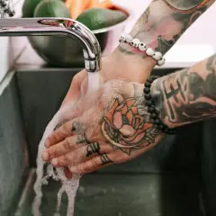 Hände mit Tattoos werden unter fließendem Wasser gewaschen, um die Pflege nach dem Duschen nach dem Tattoo zu gewährleisten.