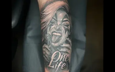 Ein detailreiches Tattoo mit einer Frau, die einen Lolli leckt, und der Aufschrift "One Life". Das Kunstwerk ist in Schwarz und Rot gehalten.
