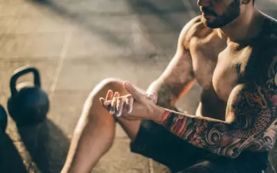 Ein Mann mit beeindruckenden herren tattoos bereitet sich mit Magnesium vor. Kettlebells liegen im Hintergrund.