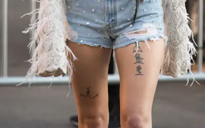 Ein Oberschenkel Tattoo Schriftzug mit einer Rose und einer stilisierten Figur.