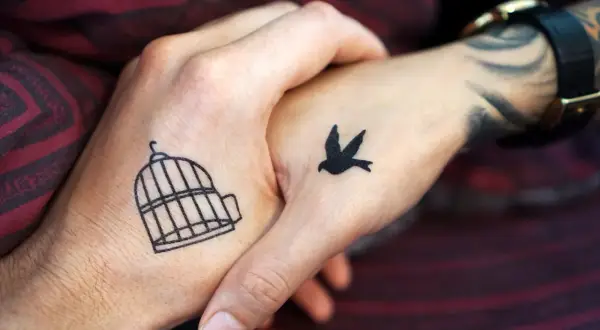 Zwei Hände mit leichten Tattoos zum selber zeichnen: Ein Vogel fliegt aus einem Käfig.