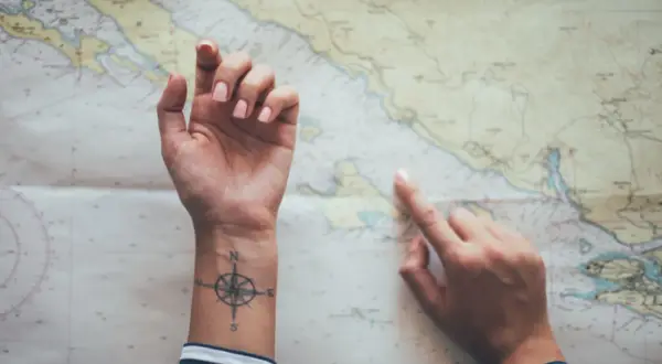 Hände über einer Seekarte, eine mit einem Kompass-Tattoo, das an ein Partner Tattoo Koordinaten erinnert.