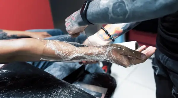 Tätowierer wickelt Arm in Folie, um das frische Tattoo zu schützen. Die Haut brennt leicht, aber das Kunstwerk wird bald sichtbar sein.