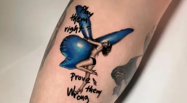 Ein Fineline Tattoo zeigt eine Frau mit Flügeln, die auf einem blauen Ballon sitzt. Darunter steht "Play them right, Prove them wrong".