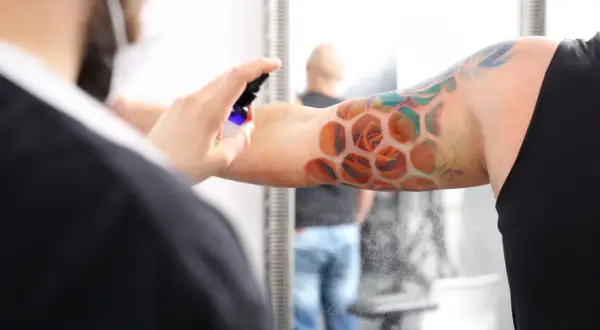 Ein frisches Tattoo mit Rosen in Wabenform wird besprüht. Der Träger ruht sich aus, während die Pflege beginnt.