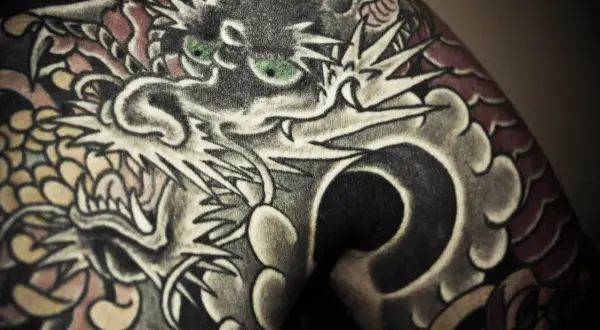 Ein detailreiches Irezumi Tattoo zeigt einen Drachenkopf mit grünen Augen, der sich über die Haut schlängelt.