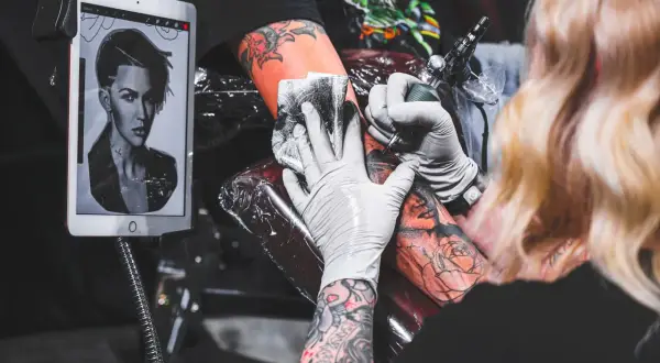 Tätowierer arbeitet an einem Porträt-Tattoo, inspiriert von kreativen Tattoos auf einem Tablet.
