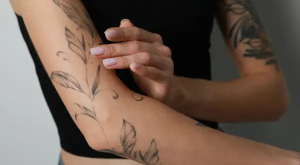 Ein frisches Tattoo mit Blattmotiven ziert den Arm einer Person, die schwarze Kleidung trägt.