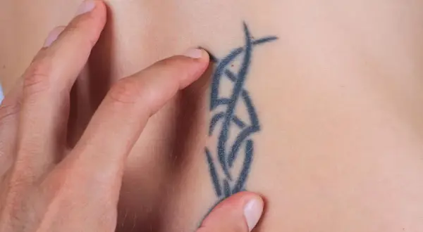 Daumen streichelt über ein Tribal-Tattoo auf der Haut einer Frau.