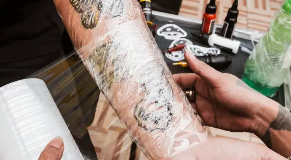 Frisch gestochenes Tattoo wird mit Tattoo-Folie geschützt. Die Folie schmiegt sich eng an, sodass keine Luft darunter ist.