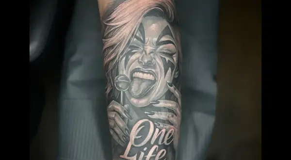 Ein detailreiches Tattoo mit einer Frau, die einen Lolli leckt, und der Aufschrift "One Life". Das Kunstwerk ist in Schwarz und Rot gehalten.