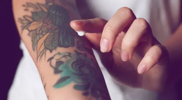 Hand testet Tattoo-Creme auf einem bunten Arm-Tattoo.